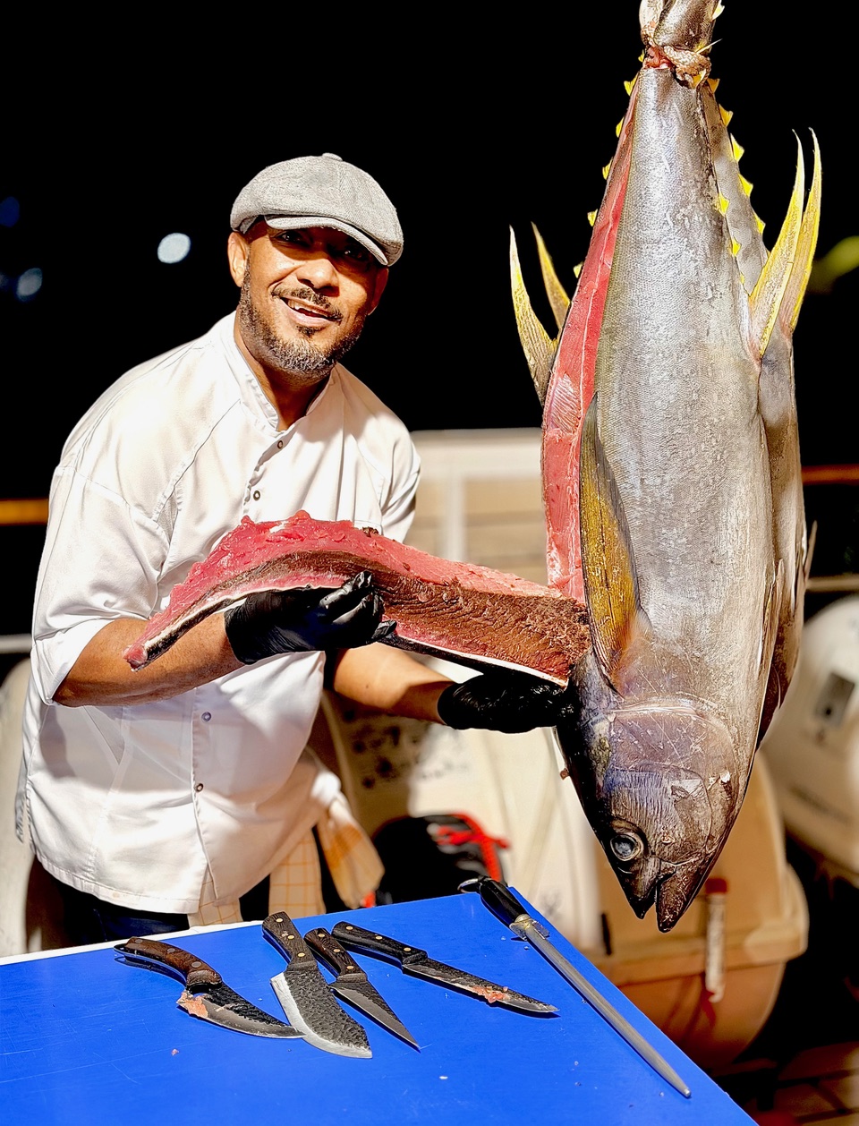 A chef holding a large yellowfin tuna on deck at night.
